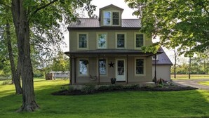 A two-story house with a front porch, a small garden, and a large tree to the left. - Your summer getaway- with a hot tub!

 (Millmont)