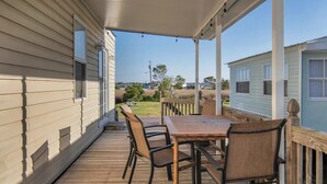 A covered porch with a wooden table and chairs, a view of a grassy area, and a small building in the background. - Surf City Cozy Home · Pets Welcome · Monthly OK (Holly Ridge)