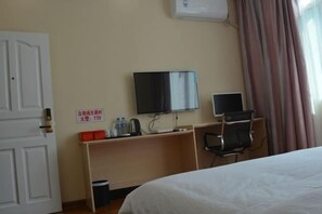 A hotel room with a bed, a desk with a computer, a TV, and a chair. There is a sign on the wall and a window with curtains. - Hongtu Business Hotel (Congjiang)