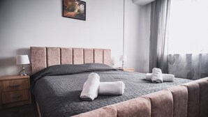 A neatly made bed with a dark quilt, a headboard, and two rolled towels on the bed. - Petrosani Camere de Inchiriat - Hotel Petroshani srl (Petrosani)