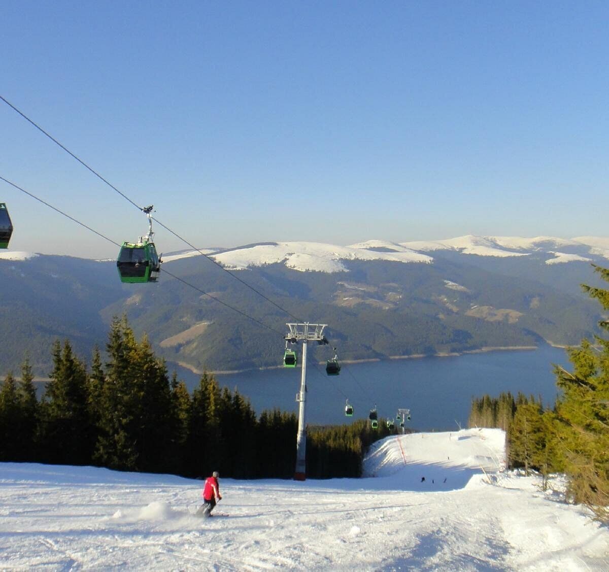 A ski lift with cabins, a skier, and a lake with mountains in the background.