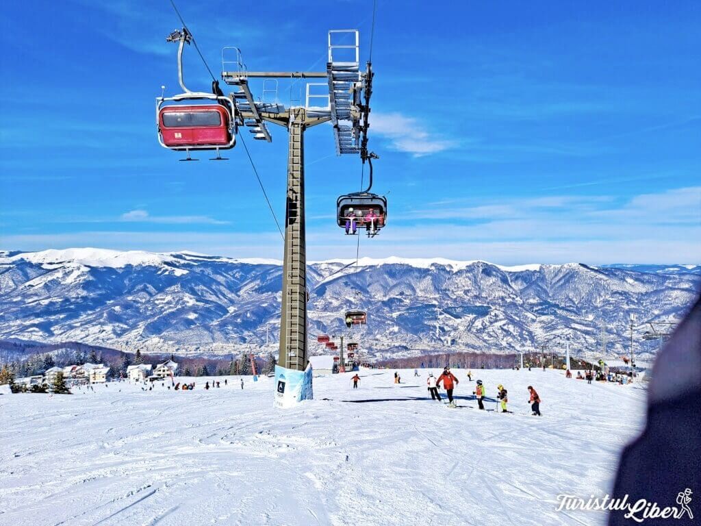 Un télésiège avec des cabines, un paysage montagneux enneigé en arrière-plan et des skieurs sur la piste.