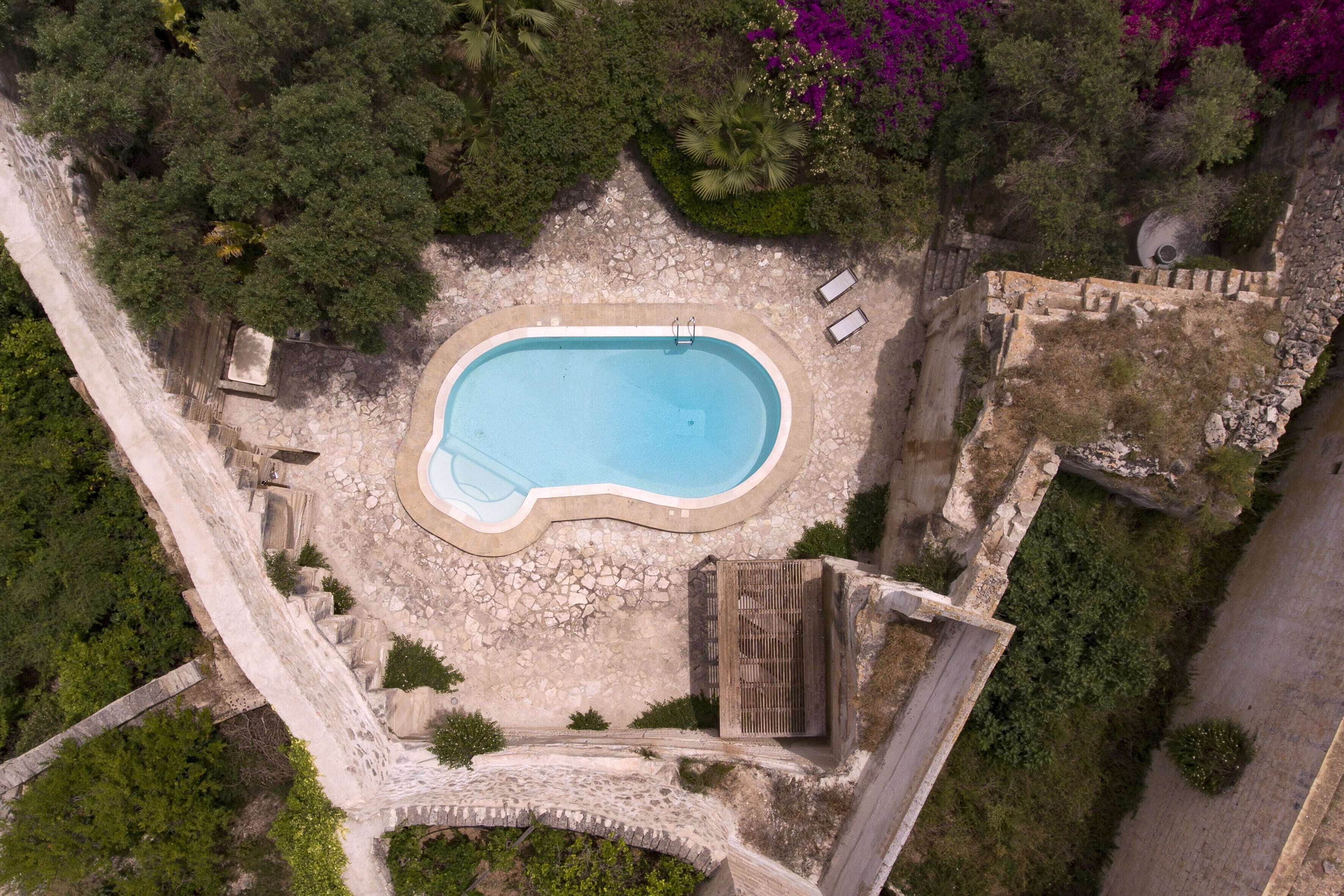Eine Vogelperspektive auf einen Swimmingpool, umgeben von Steinmauern und üppiger Vegetation.