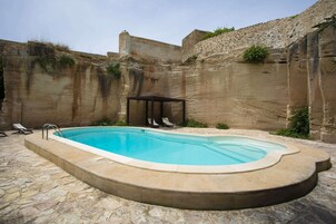 Piscina con borde de piedra, una tumbona y una zona de estar cubierta.