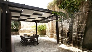 Un espace extérieur abrité, aménagé pour les repas, avec un sol en pierre et une table dressée pour quatre personnes.