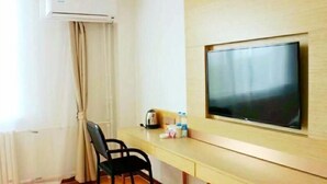A hotel room with a wooden desk, a black chair, a flat-screen TV mounted on the wall, an air conditioning unit, and a window with curtains. - Green Tree Inn Yantai Zhifu Donglu Branch (Yantai)