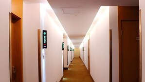 A hotel corridor with doors marked by illuminated signs, a carpeted floor, and a ceiling light fixture. - Green Tree Inn Yantai Zhifu Donglu Branch (Yantai)