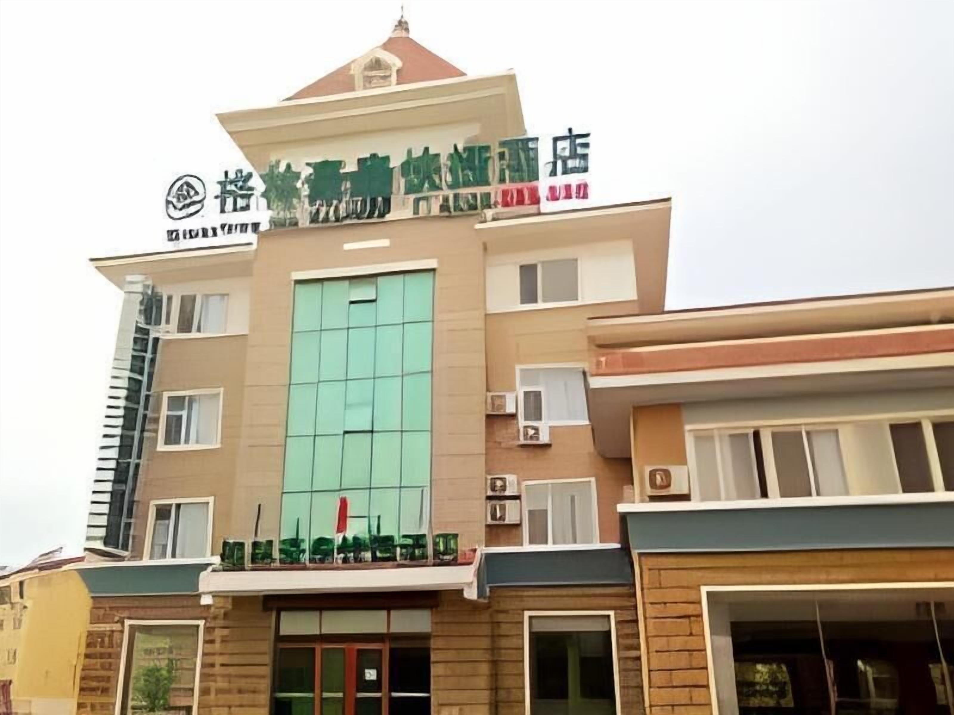A hotel with a modern design, featuring a prominent green sign with Chinese characters, multiple windows, and a flat roof.