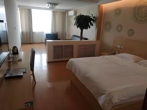 A hotel room with a large bed, a desk with a chair, a plant, and a wall with circular patterns. - Green Tree Inn Yantai Zhifu Donglu Branch (Yantai)