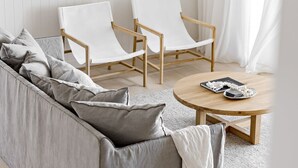 A modern living room with a grey sofa, two white armchairs, a wooden coffee table, and a white rug. - The Palm House Gerroa (Gerroa)