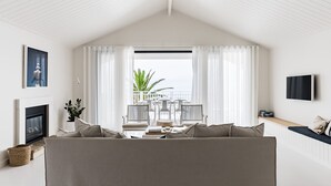 A cozy living room with a large window, a fireplace, and a TV mounted on the wall. - The Palm House Gerroa (Gerroa)