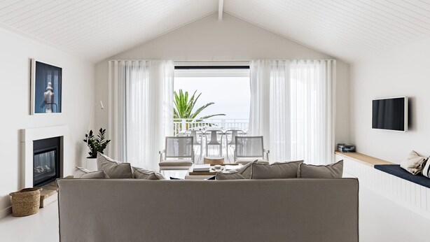 A cozy living room with a large window, a fireplace, and a TV mounted on the wall. - The Palm House Gerroa (Gerroa)