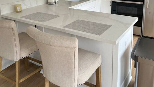 A modern kitchen with white cabinetry, a central island with bar stools, a microwave, a coffee maker, and a kettle.