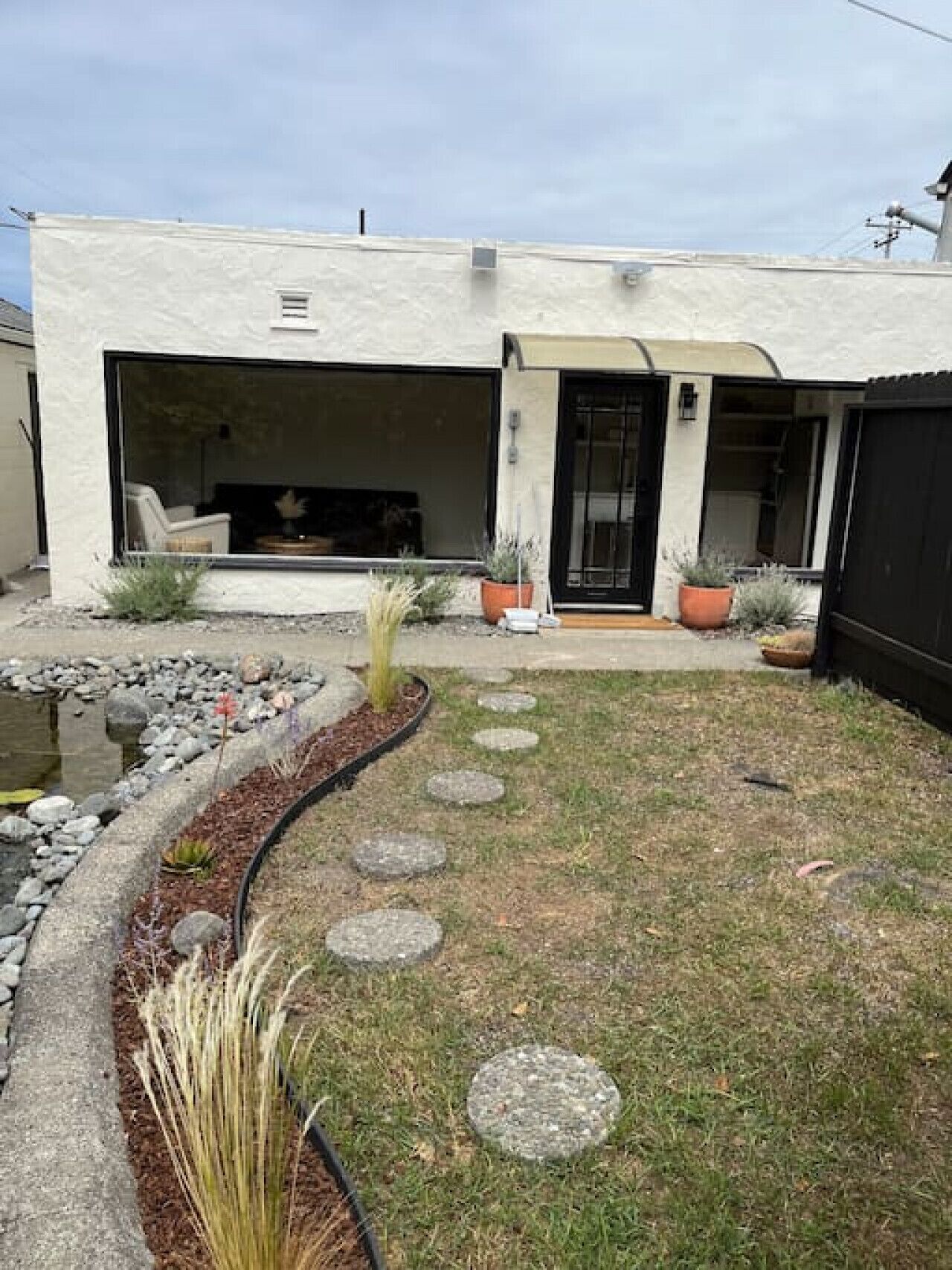 Una casa moderna con un amplio patio abierto, un camino de piedra y plantas en macetas.