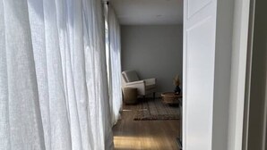 A hallway with a wooden floor, white walls, and a chair in the distance.