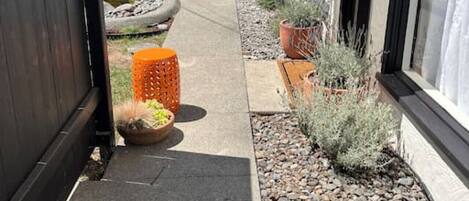 A narrow pathway leading to a house with a black gate, potted plants, and a small garden area with gravel and rocks.