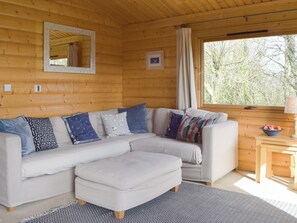 A log cabin interior with a sofa, ottoman, and a small table with a bowl of fruit.