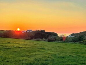 Un atardecer sobre un campo cubierto de hierba, con una casa en una colina.