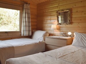 Een kamer in chaletstijl met twee bedden, een raam met gordijnen, een spiegel en een bedlampje.