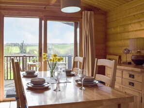 Une table à manger en bois, dressée avec des assiettes, des bols et des verres à vin, donnant sur un paysage verdoyant.