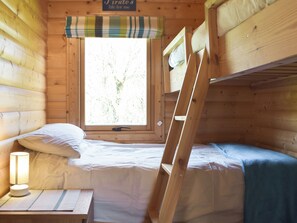 A cabin with bunk beds, a window with a view of trees, a lamp on a bedside table, and a sign above the window.