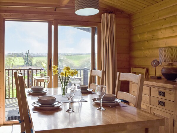 A wooden dining table set with plates, bowls, and wine glasses, with a view of greenery outside.