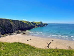 Un paysage côtier avec une plage de sable, des falaises verdoyantes et un ciel bleu dégagé.