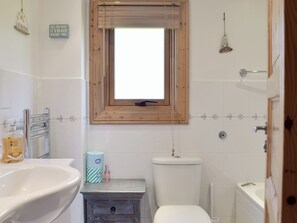 A bathroom with a wooden-framed window, a white sink, a toilet, and a small vanity with a towel holder.