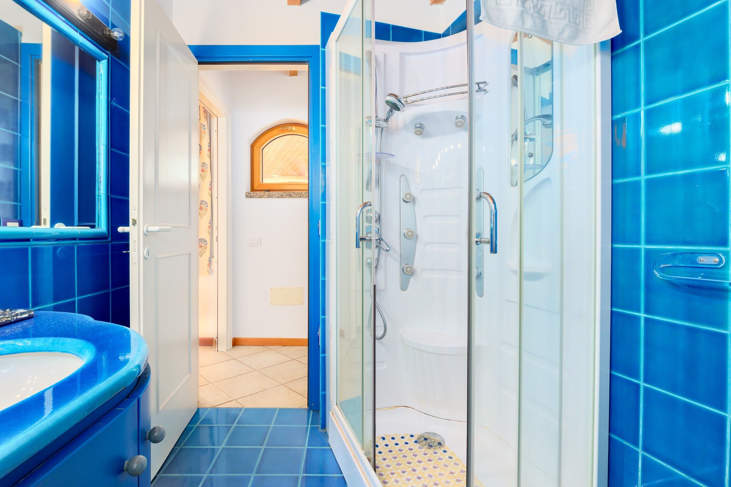 Un baño con pared de azulejos azules, ducha con mampara de vidrio y lavamanos.