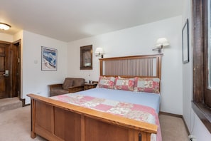 Une chambre à coucher avec un lit en bois, une table de chevet, une chaise, une lampe et une affiche accrochée au mur.