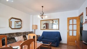 Ein Wohnzimmer mit einem blauen Sofa, einem Holzesstisch, Stühlen, einer Chandelier und einem großen Spiegel an der Wand.
