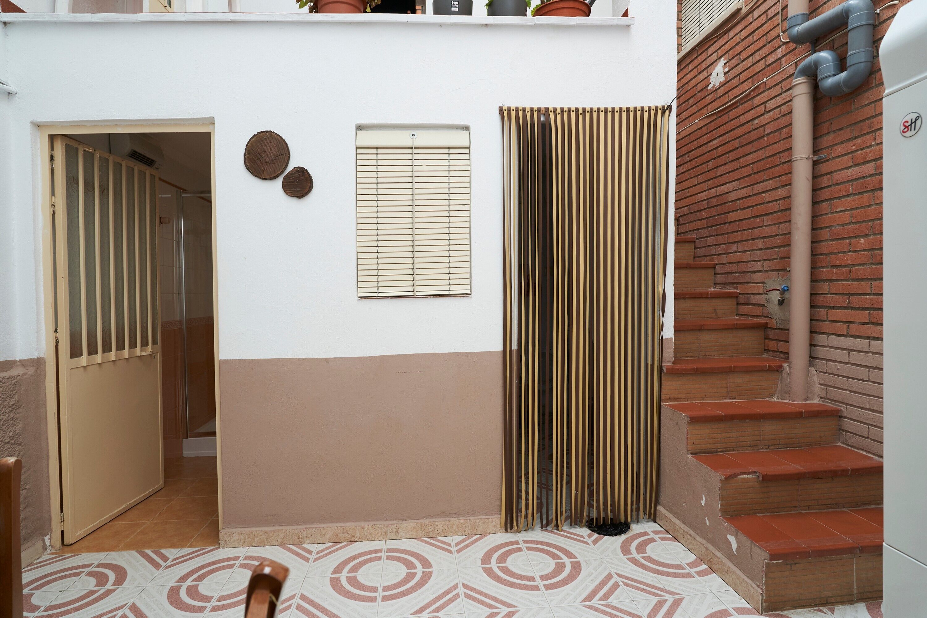 A hallway with a door, a window with blinds, a striped curtain, and a staircase with red steps.