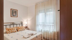 Ein Schlafzimmer mit Bett, Nachttisch, Lampe, gerahmtem Bild an der Wand und einem Fenster mit Vorhängen.