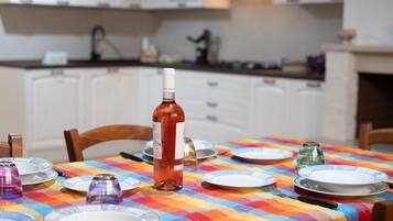 Ein Esszimmertisch ist gedeckt mit Tellern, einer Weinflasche und einer bunten Tischdecke in einer Küche mit weißen Schränken und einem Herd.