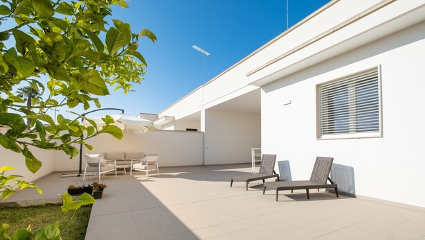 Un patio moderno al aire libre con un muro blanco, una ventana con persianas y dos sillones de relax.