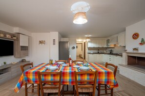 A dining area with a table set for six, a television, and a kitchen in the background.