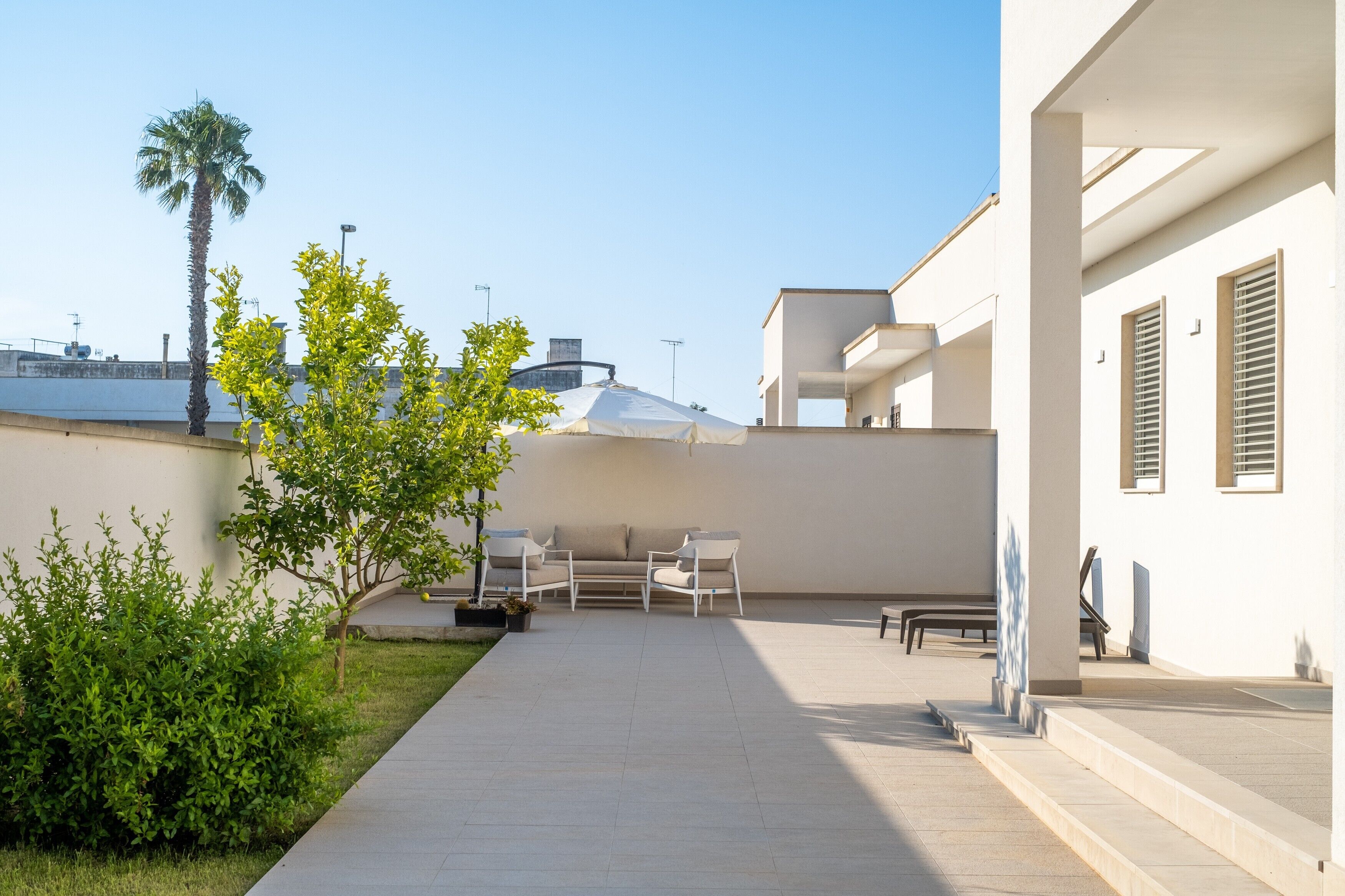 Une terrasse extérieure moderne, dotée d’un canapé et de fauteuils, d’un palmier et offrant une vue sur la mer.