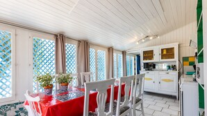 A dining area with a red tablecloth, white chairs, and potted plants.