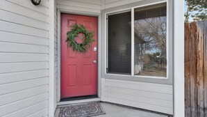 Una puerta roja con un adorno de corona, una ventana con mosquitero y una pared exterior blanca.