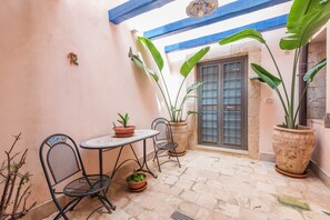 A small patio area with a table and chairs, potted plants, and a door with a window.