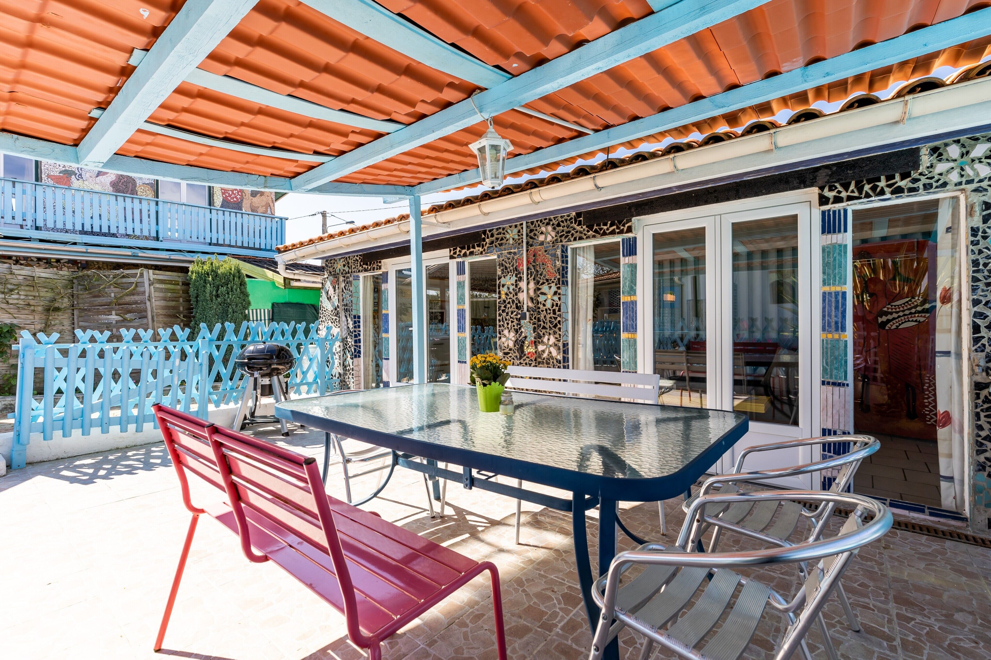 An outdoor patio with a glass table, metal chairs, and a red bench.