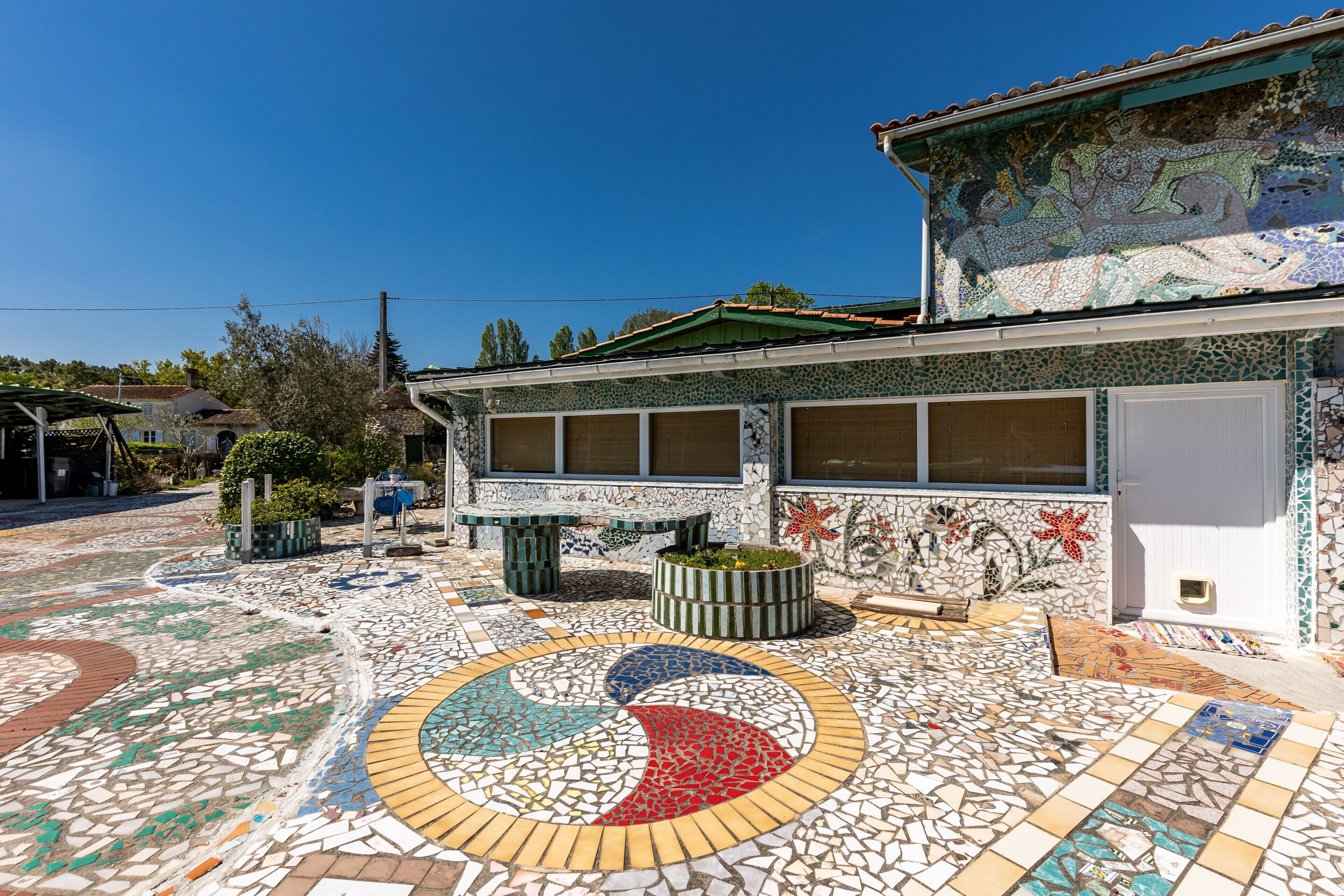 Un bâtiment doté d’une cour dallée, ornée d’une mosaïque circulaire, de grandes fenêtres et d’un toit végétalisé.