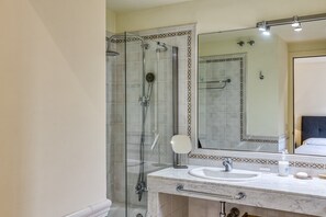 Een badkamer met een douchecabine van glas, een marmeren wastafel en een grote spiegel.