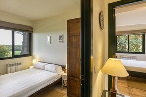 Une chambre à coucher comprenant un lit, une table de chevet, une lampe, une porte en bois et une fenêtre donnant sur un paysage verdoyant.