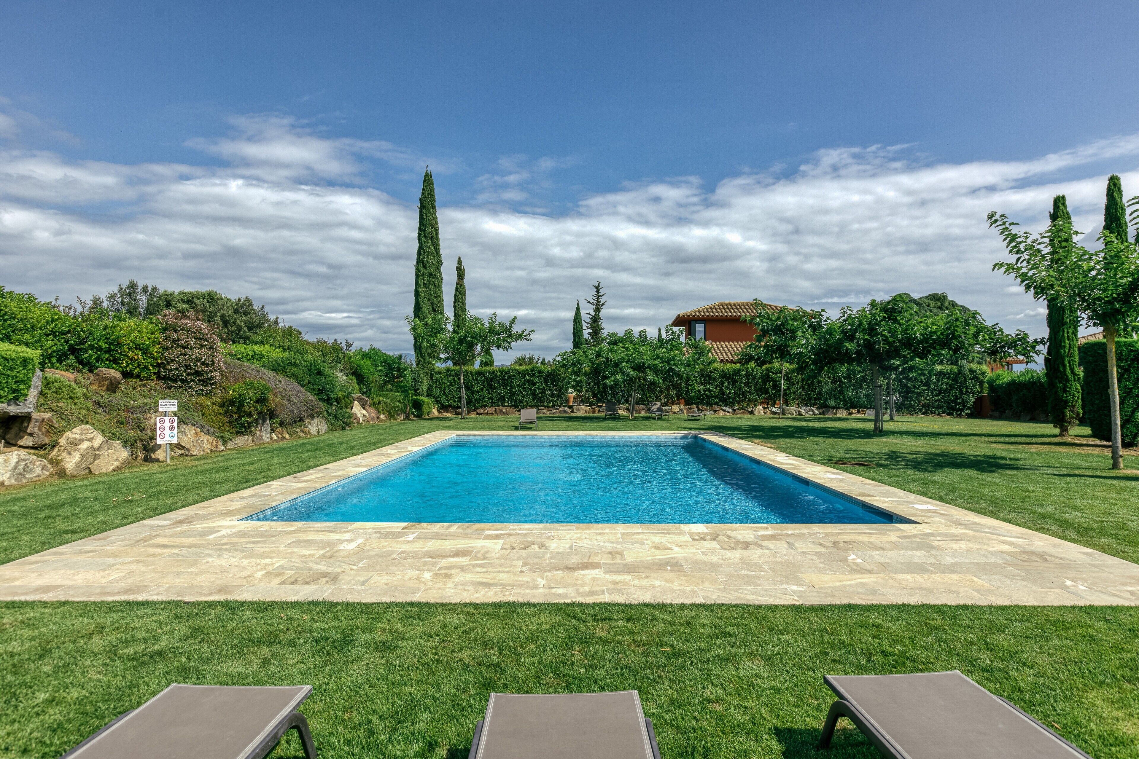A rectangular swimming pool with a stone border, surrounded by well-maintained grass, and a clear blue sky.