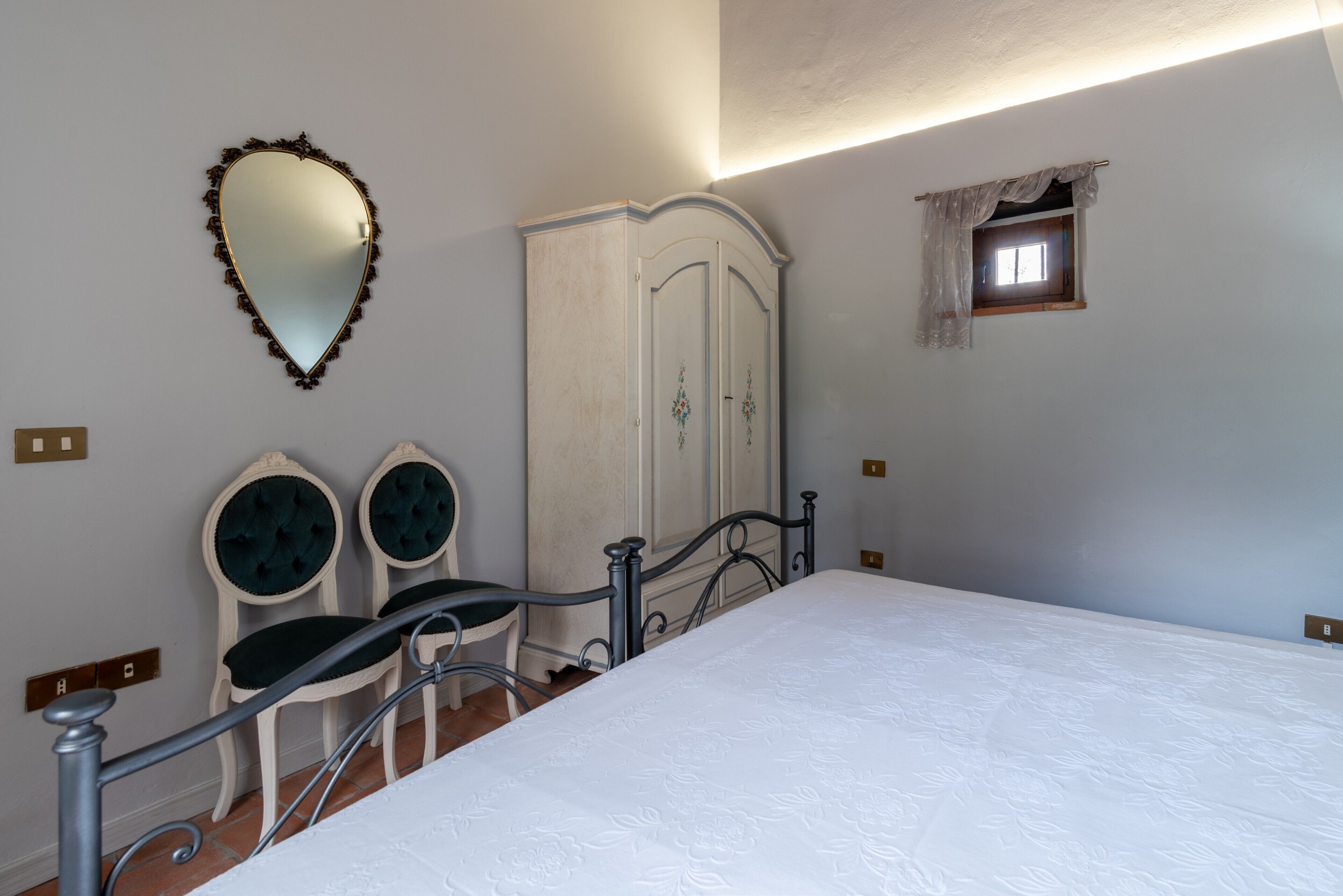 Un dormitorio con cama, dos sillas, un armario, un espejo y una ventana.