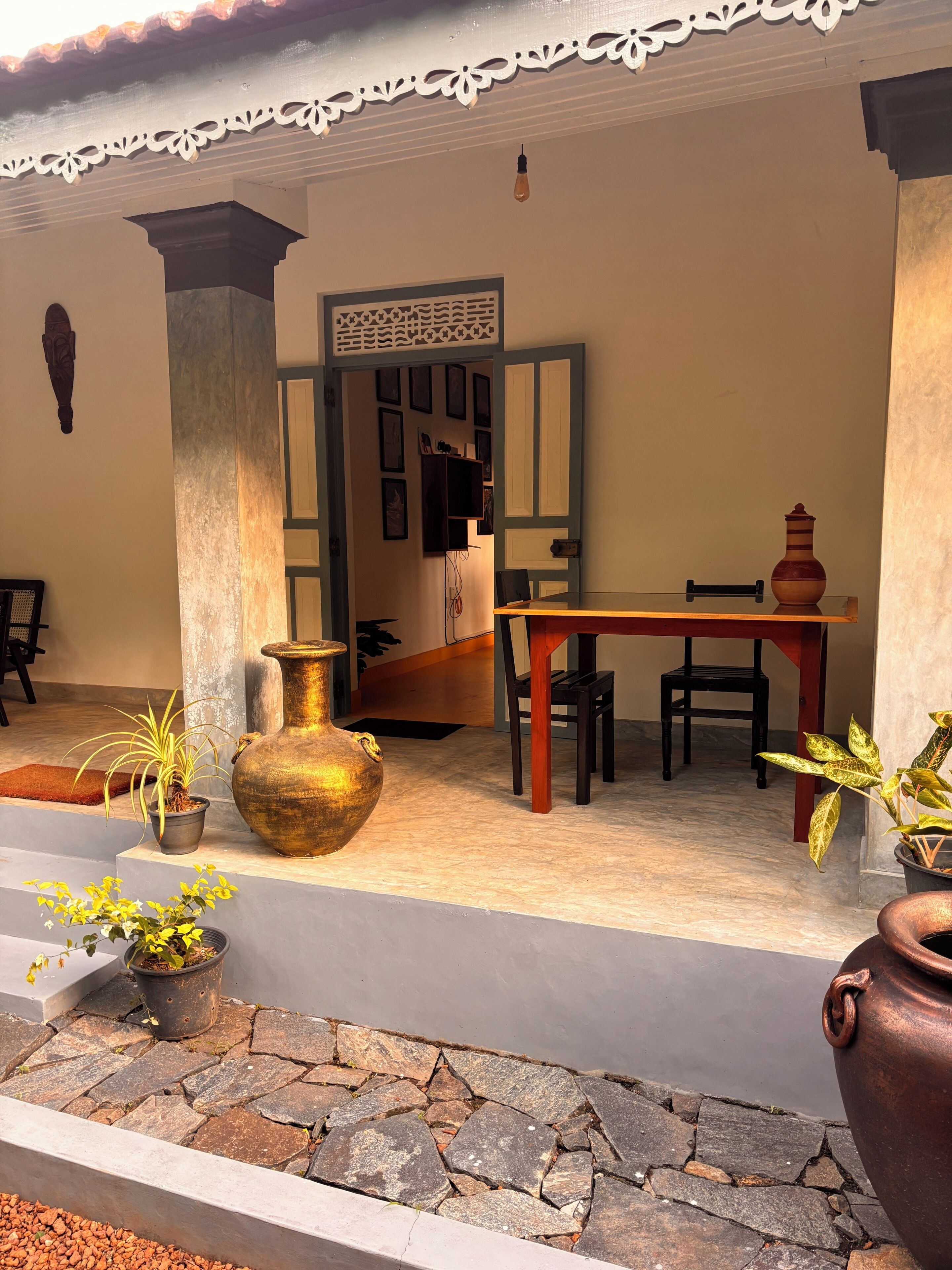 A covered outdoor area with a table and chairs, potted plants, and a decorative vase.