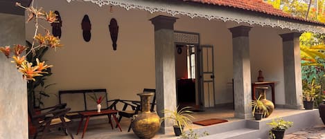 A traditional house with a tiled roof, a porch with a bench, and potted plants.