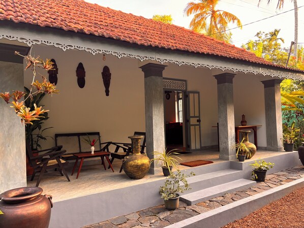 A traditional house with a tiled roof, a porch with a bench, and potted plants.