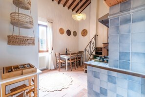Een keuken met een betegelde achterwand, houten stoelen, een eettafel, hangmanden en een trap.